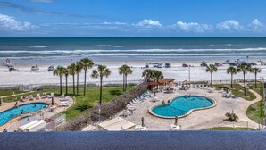 A beach resort with a swimming pool, lounge chairs, and a view of the ocean.