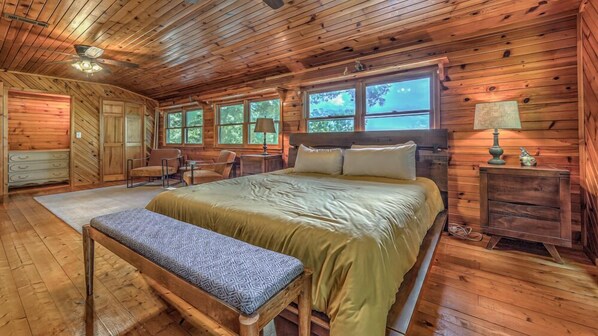 A wooden cabin bedroom with a bed, bench, dresser, and windows.