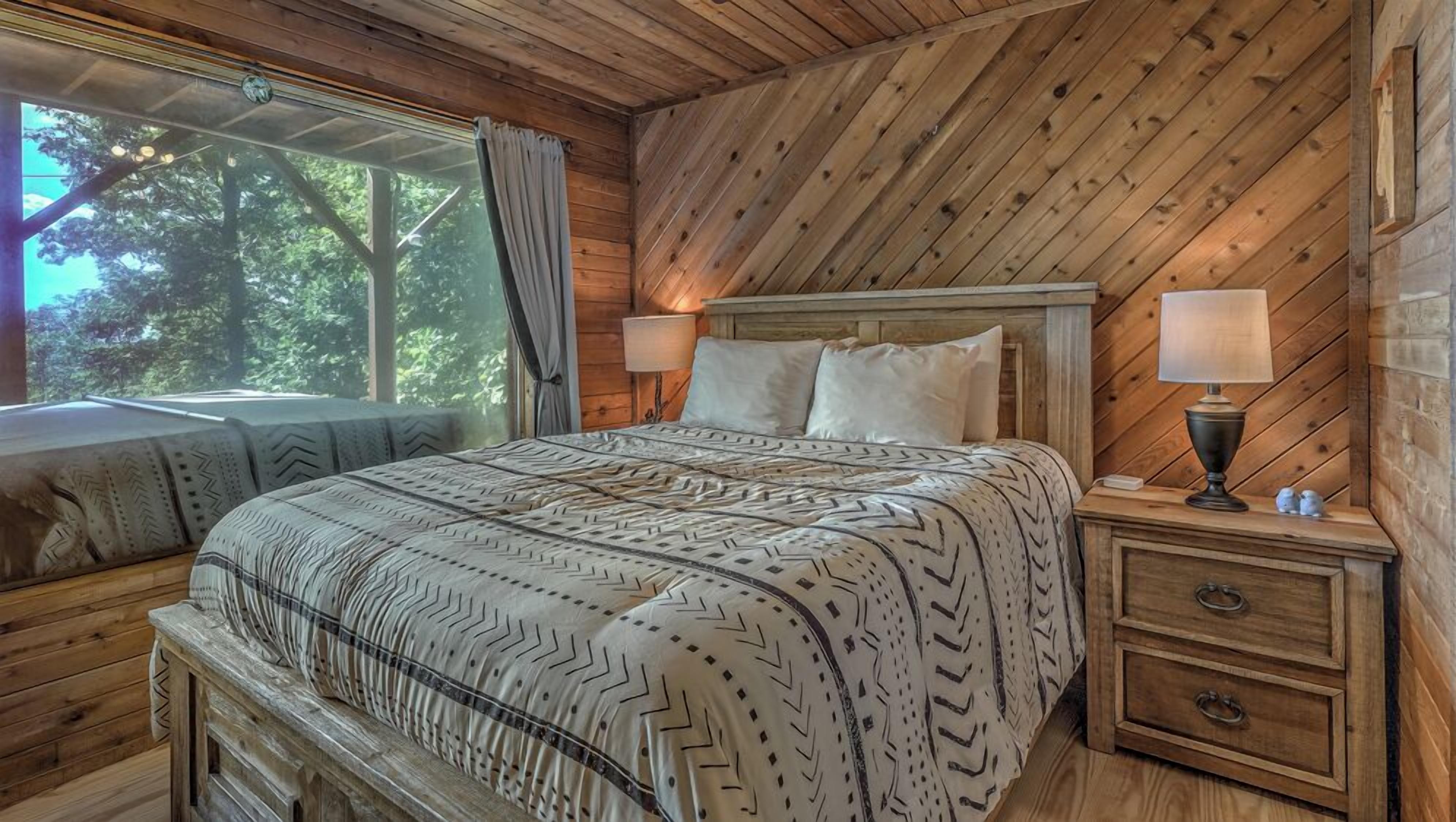 Een slaapkamer in een houten blokhut met een bed, twee bedlampjes, een nachtkastje en een raam met gordijnen.