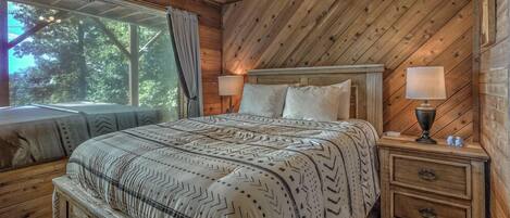 Een slaapkamer in een houten blokhut met een bed, twee bedlampjes, een nachtkastje en een raam met gordijnen.