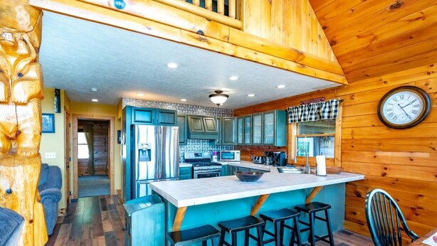 A kitchen with a central island, bar stools, a clock, and wooden walls.