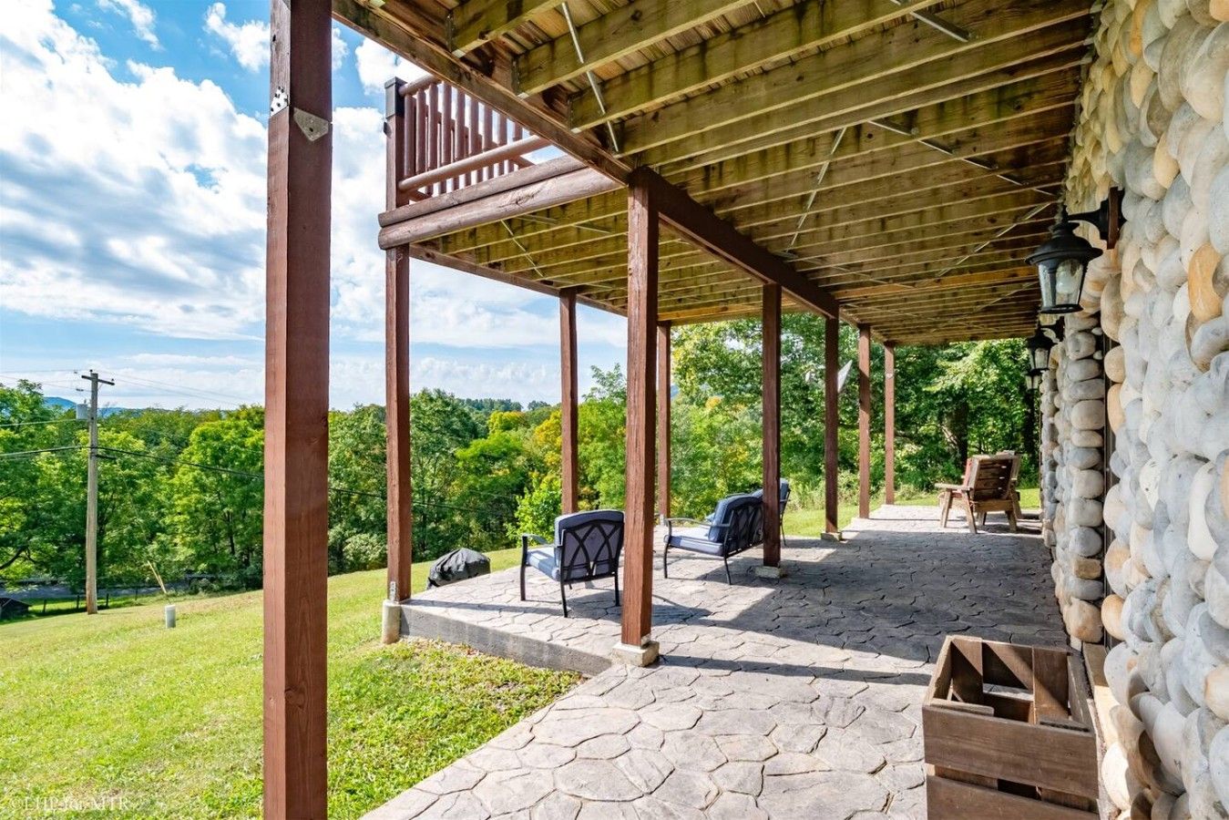 A covered outdoor area with stone flooring, wooden pillars, and a stone wall.