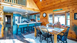 A wooden cabin interior with a kitchen, dining area, and a staircase leading to an upper level. - Panoramic Point - 91 Panoramic Drive (Dryfork)