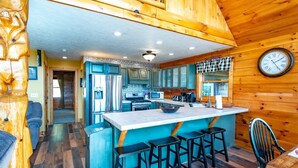 A log cabin interior with a kitchen featuring a central island, bar stools, and a wooden ceiling. - Panoramic Point - 91 Panoramic Drive (Dryfork)