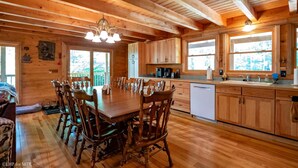 A wooden cabin interior with a dining table, chairs, kitchen area, and windows. - Countless Adventures (Davis)