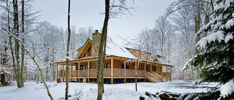 A wooden cabin with a porch, surrounded by snow-covered trees.