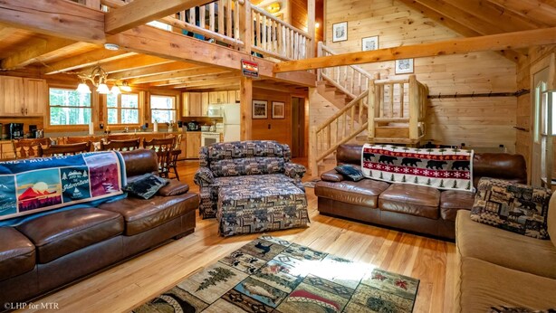 A cozy log cabin interior with a dining area, a staircase, and a living room furnished with leather sofas and patterned rugs. - Countless Adventures (Davis)