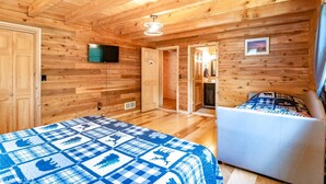 A wooden cabin room with a bed, a chair, a television, and a door leading to another room. - Countless Adventures (Davis)