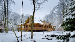 A wooden cabin with a balcony, surrounded by snow-covered trees. - Countless Adventures (Davis)