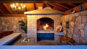 A stone fireplace with a fire, wooden beams, and a chandelier. - Villa Silente (Oklaj)
