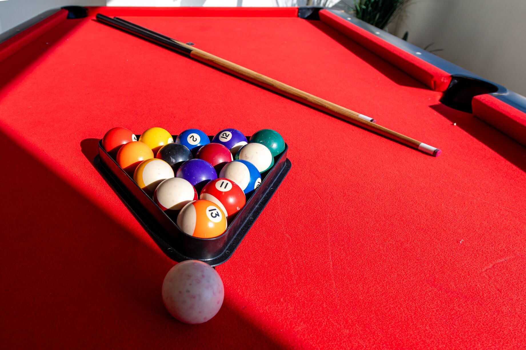 A pool table with a red felt surface, a pool cue, and a rack of billiard balls.