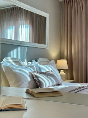 Quarto de hotel com cama, abajur, espelho e janela com cortinas.