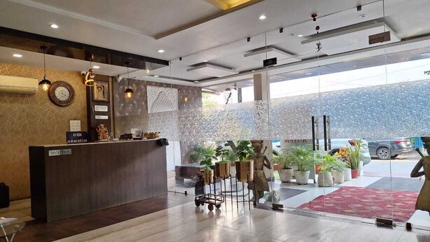 A modern hotel lobby with a reception desk, potted plants, and a view of the street outside. - Hotel Mayur Palace (Bhopal)