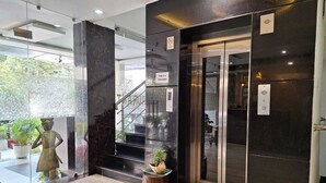 A modern lobby with a glass wall, a statue, a staircase, and a sign indicating elevator access for 4 persons. - Hotel Mayur Palace (Bhopal)