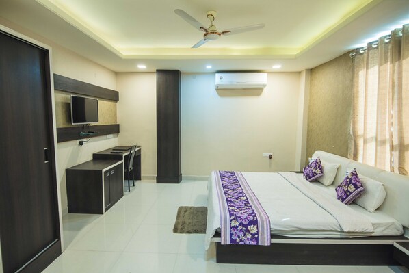 A bedroom with a bed, a desk, a chair, a television, and an air conditioning unit. - Hotel Mayur Palace (Bhopal)