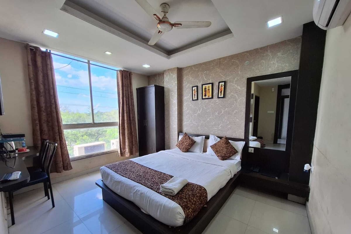 A hotel room with a large bed, a desk, a chair, and a wardrobe.