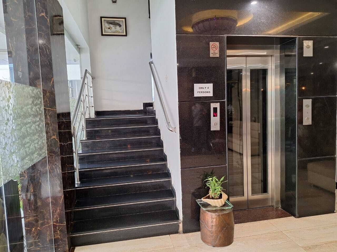 A staircase leading to an elevator with a 'Only 4 Persons' sign, a potted plant, and a marble wall.