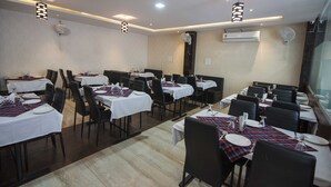 A restaurant with multiple tables, black chairs, and white tablecloths. - Hotel Mayur Palace (Bhopal)