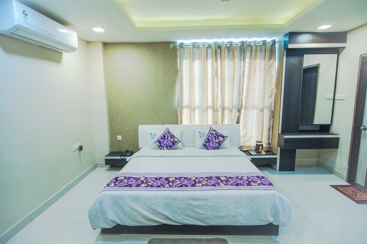 A hotel room with a bed, nightstands, an air conditioner, a mirror, and a curtain.