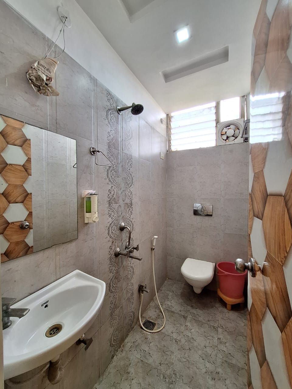 A bathroom with a sink, mirror, shower, toilet, and a red bucket.
