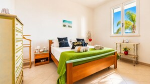 A bedroom with a bed, a nightstand, a dresser, a window with a view, and a bedside table with a lamp.