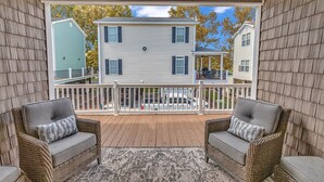 A covered porch with wicker furniture and a view of a two-story house. - Vacation home in Ocean lakes at Myrtle beach (Myrtle Beach)