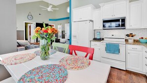 A modern kitchen with white cabinets, a microwave, and a stove. There is a dining table with colorful placemats and a vase of flowers. - Vacation home in Ocean lakes at Myrtle beach (Myrtle Beach)