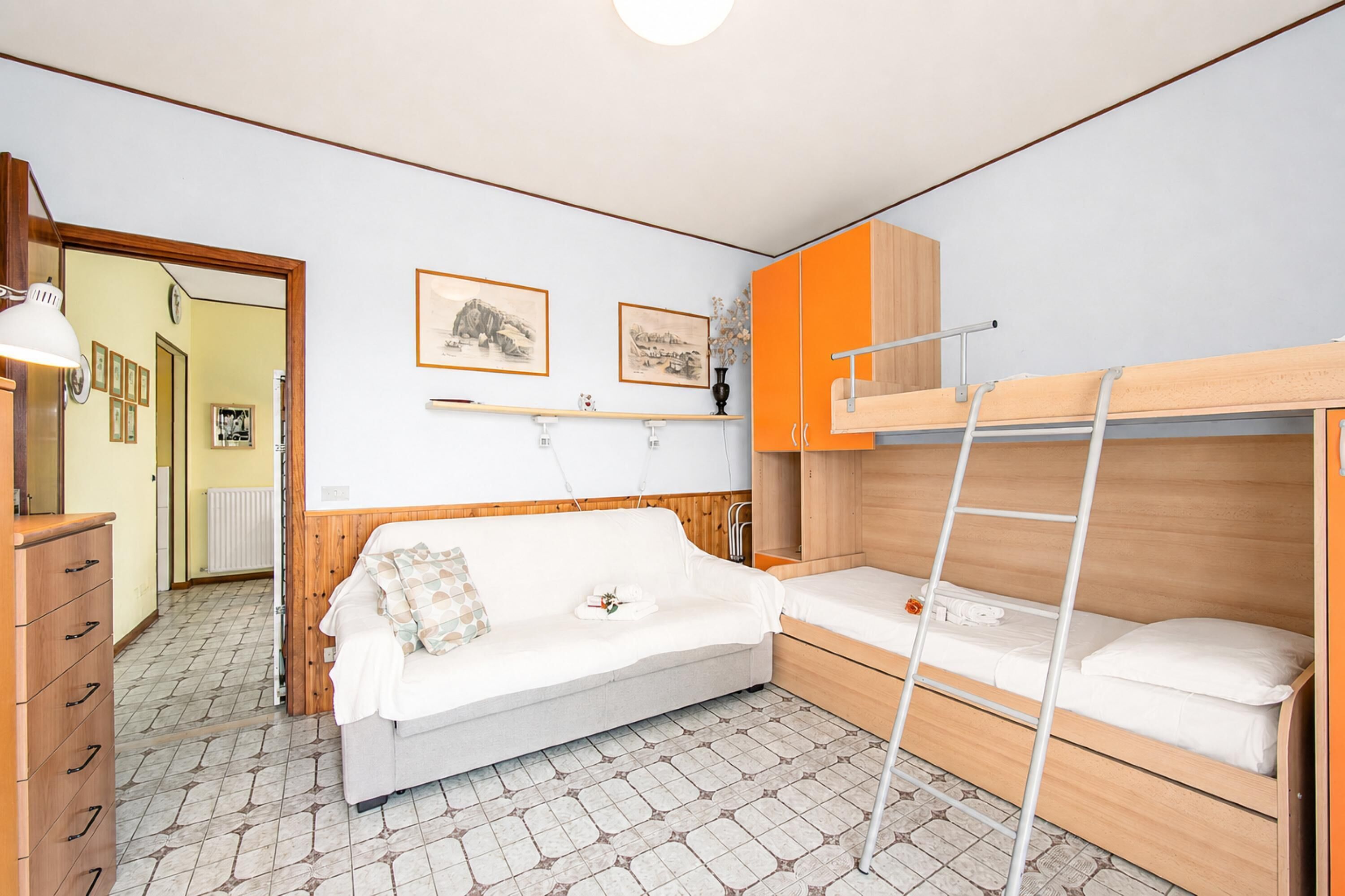 Een kleine kamer met een stapelbed, een slaapbank, een dressoir en een spiegel.
