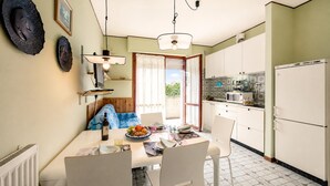 Een eetgedeelte met een tafel voor vier personen, een keuken met witte kasten, en uitzicht door een raam.