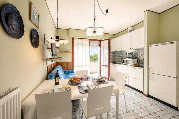 A dining area with a table set for four, a kitchen with white cabinets, and a view through a window.