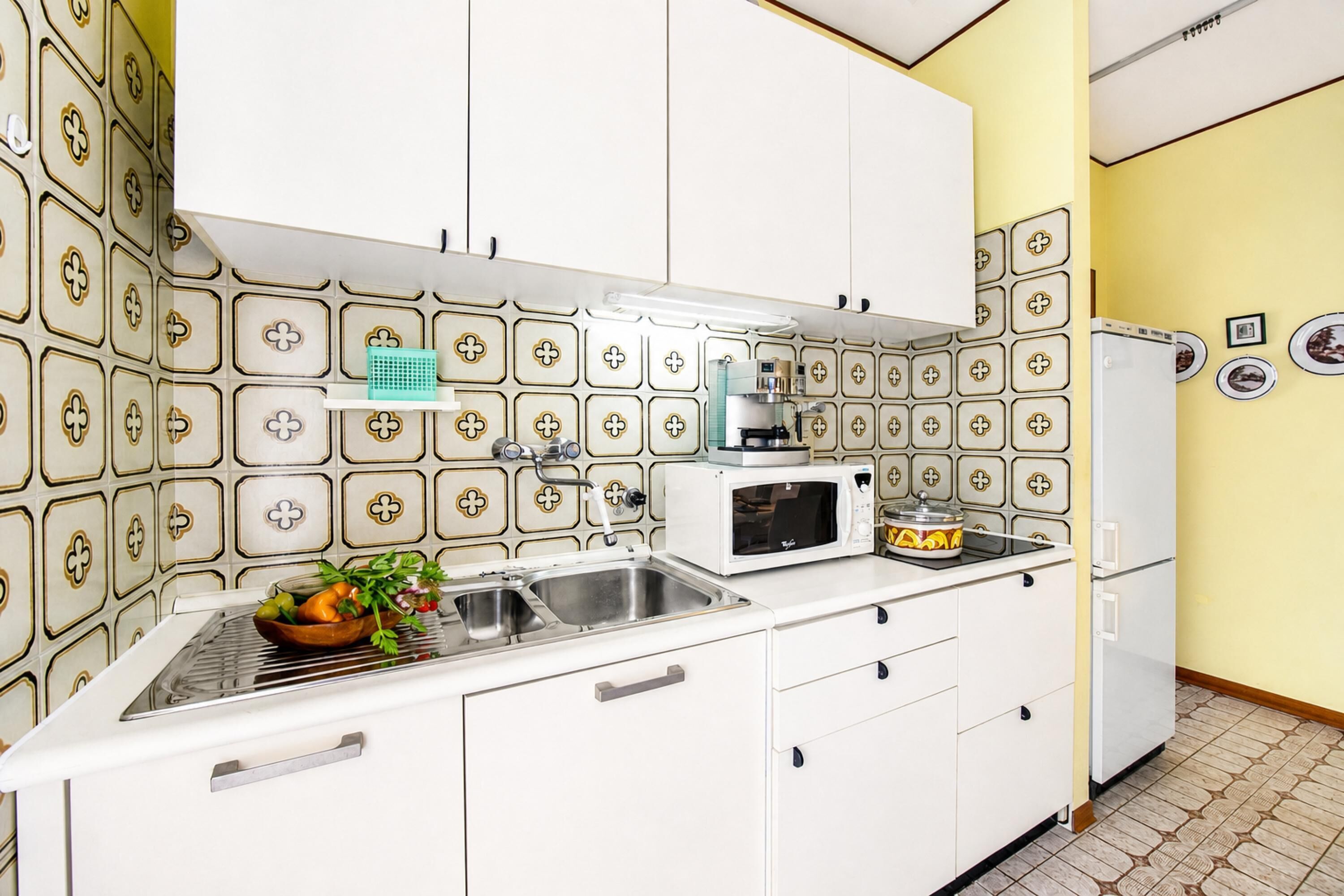 A kitchen with white cabinets, a microwave, a sink, and a patterned backsplash.