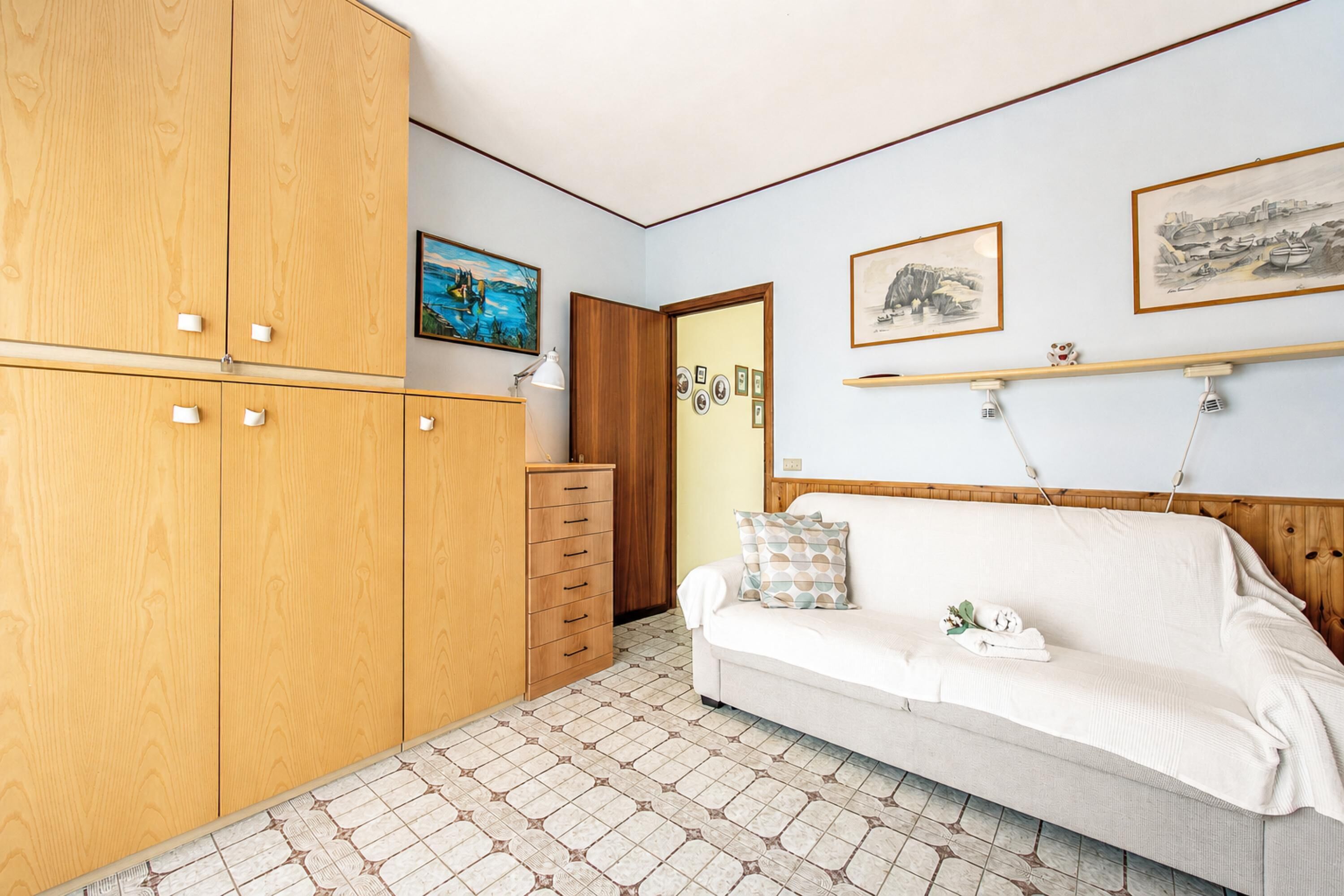 Una habitación con un armario de madera, un sofá blanco, suelo de baldosas y cuadros en la pared.