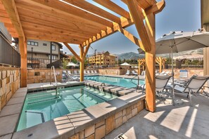 Zona de piscina con pérgolas de madera, sillas de descanso y vistas a edificios y montañas al fondo.