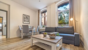 Una sala de estar moderna con sofá, mesa de comedor y un ventanal con cortinas.
