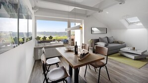 A modern living space with a dining area, a sofa, and a view of the outdoors. - Studio Apartment: Loft with Lake View (Petersthal)