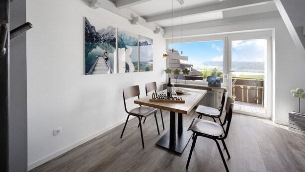 A modern dining area with a wooden table, four chairs, and a 'Welcome' sign. - Studio Apartment: Loft with Lake View (Petersthal)
