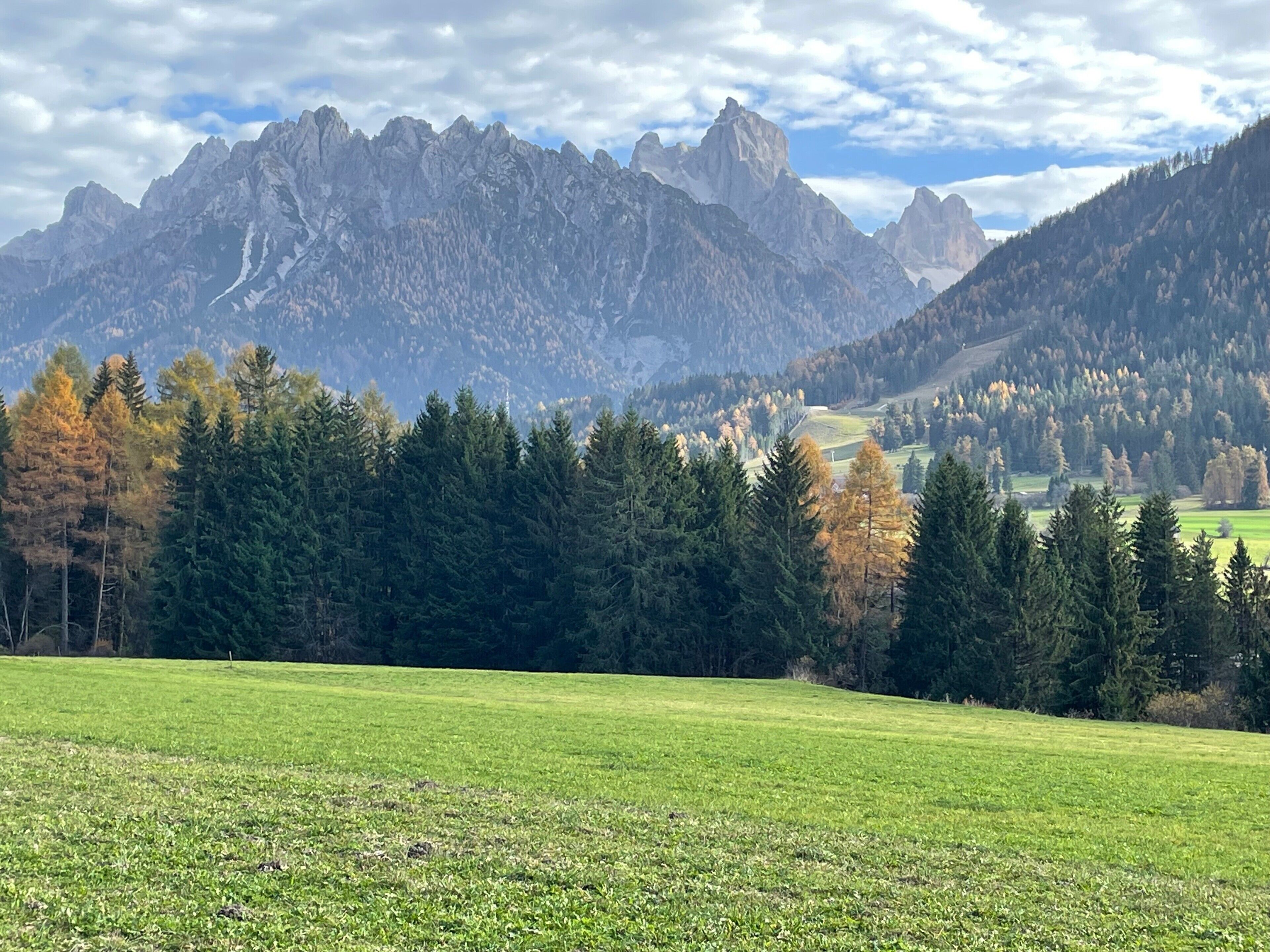 A mountainous landscape with a field in the foreground and a valley with trees and buildings in the background.