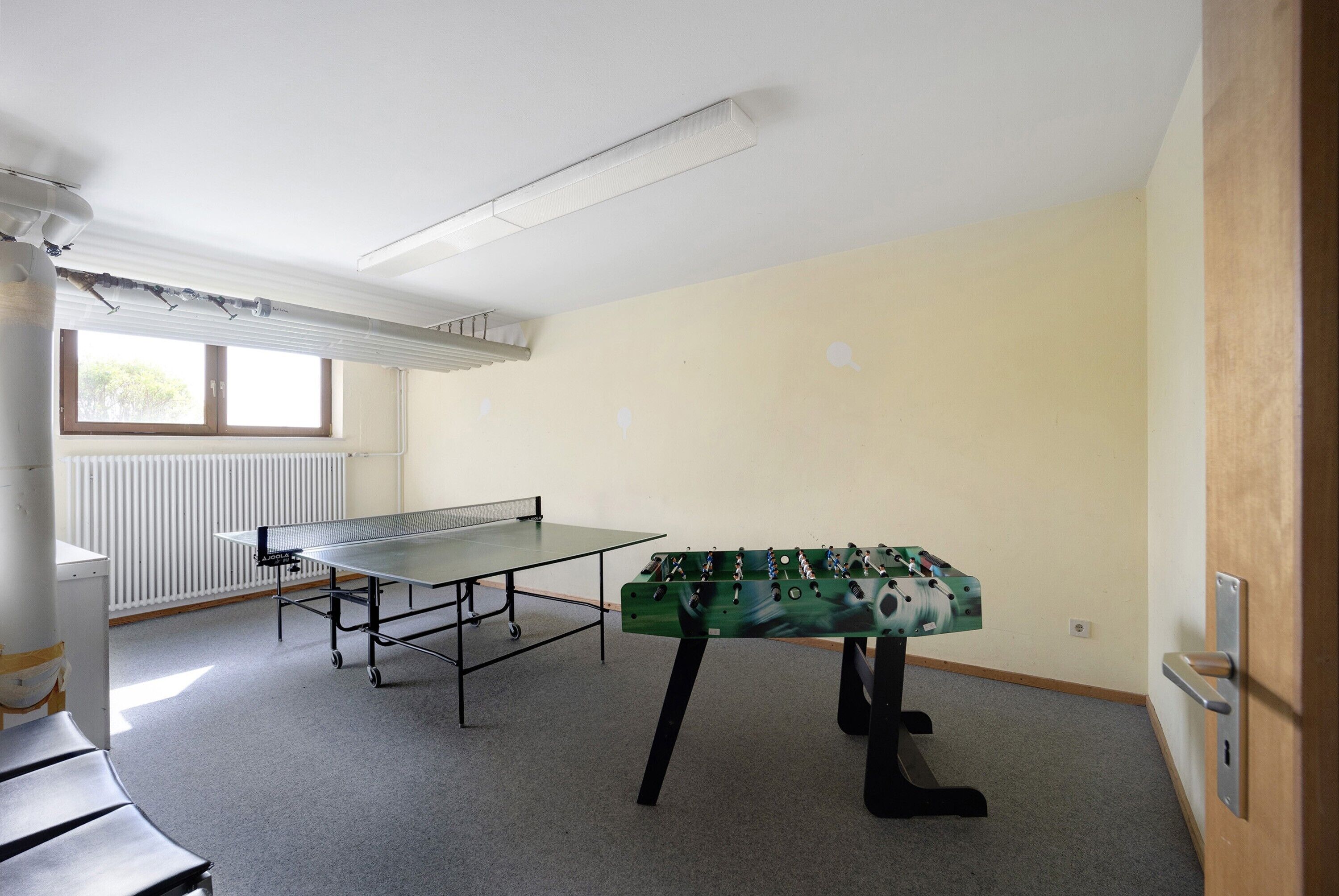 Una habitación con mesa de ping pong, mesa de fútbol de mesa, radiador y ventana.