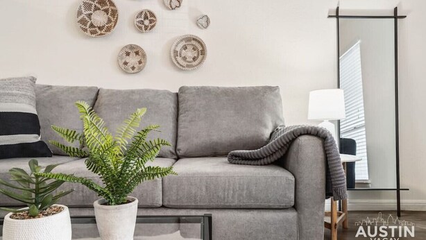 Un salon moderne avec un canapé gris, une table basse en verre et des œuvres d’art décoratives accrochées au mur.