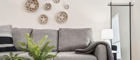 Un salon moderne avec un canapé gris, une table basse en verre et des œuvres d’art décoratives accrochées au mur.