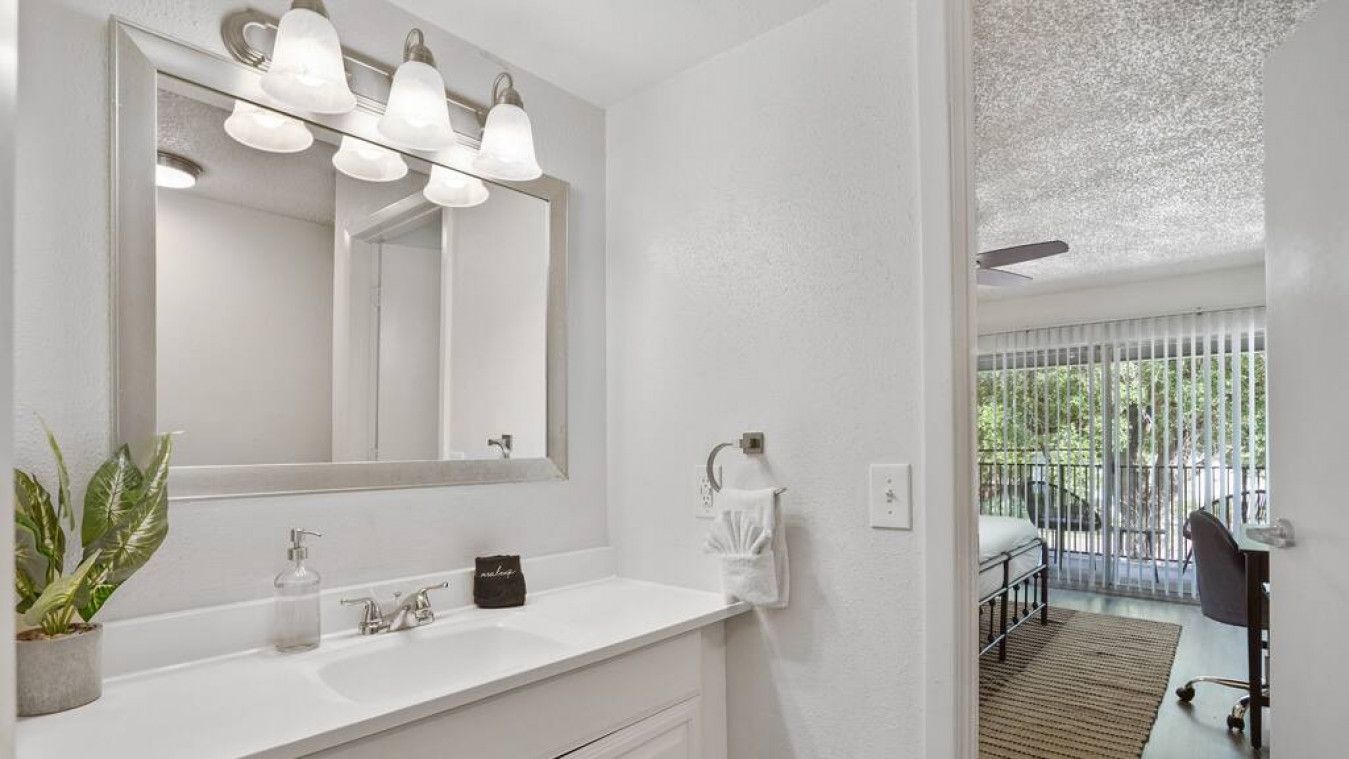 A modern bathroom with a white vanity, a large mirror, and a plant.