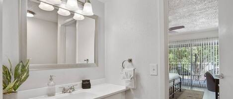 A modern bathroom with a white vanity, a large mirror, and a plant.