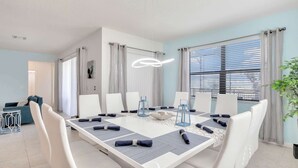 Une salle à manger moderne avec une table blanche dressée pour six personnes, entourée de chaises blanches.
