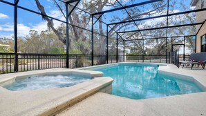 Une piscine avec un jacuzzi, entourée d’une zone couverte dotée d’une structure métallique et de murs en verre.