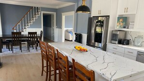 A modern kitchen with a marble countertop, stainless steel appliances, and wooden chairs. - Peaceful retreat with fully stocked kitchen. (Redlands)