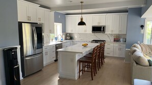 A modern kitchen with white cabinets, stainless steel appliances, a central island with bar stools, and a built-in microwave. - Peaceful retreat with fully stocked kitchen. (Redlands)