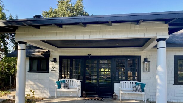 A covered porch with two white benches, a black door, and a white fence. - Peaceful retreat with fully stocked kitchen. (Redlands)