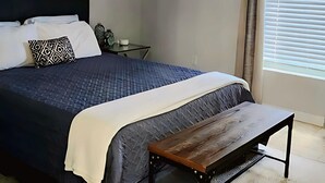 Ein Schlafzimmer mit Bett, Nachttisch, Bank, Deckenventilator und einem Fenster mit Jalousien.