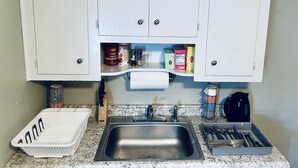 A kitchen with white cabinets, a stainless steel sink, and various kitchen items like a dish rack, knife block, and spice containers. - Luxury 2 bedroom 🛌 Next to UBS Arena🏟 & JFK✈️ (Valley Stream)