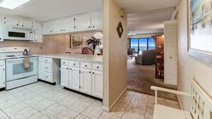 A kitchen with white cabinets, a microwave, and a stove. There is a dining area with a chair and a table. - Ocean view from the master bedroom and living room with a spacious balcony (Fernandina Beach)